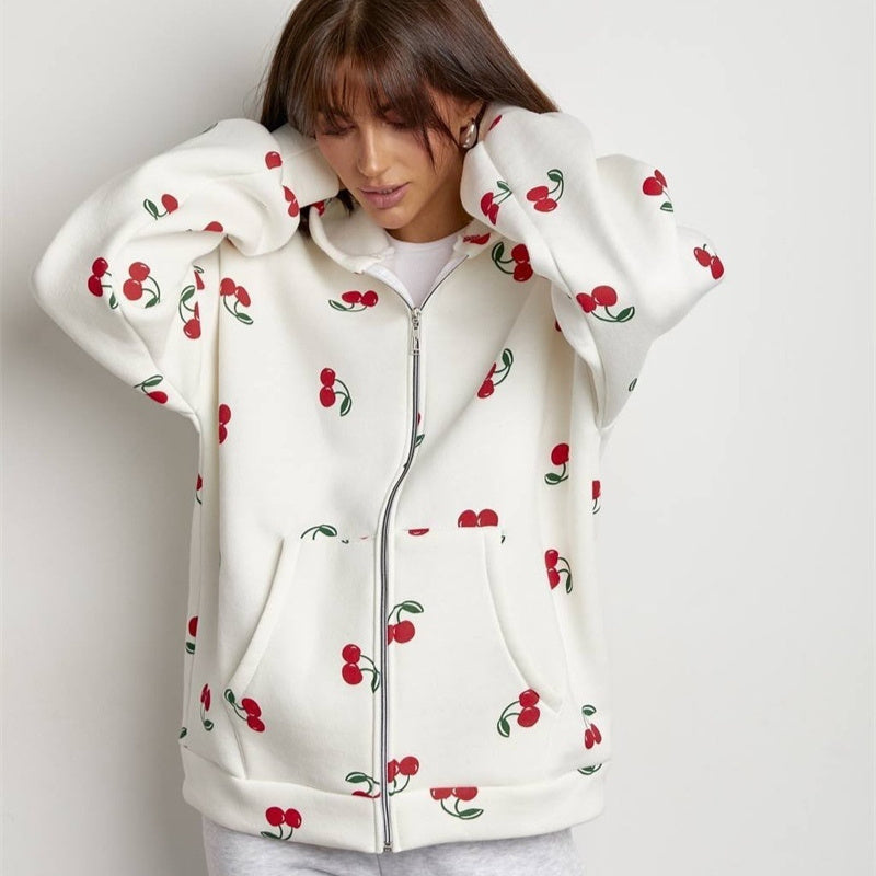 White hoodie with red cherry pattern worn by a person on a light gray background