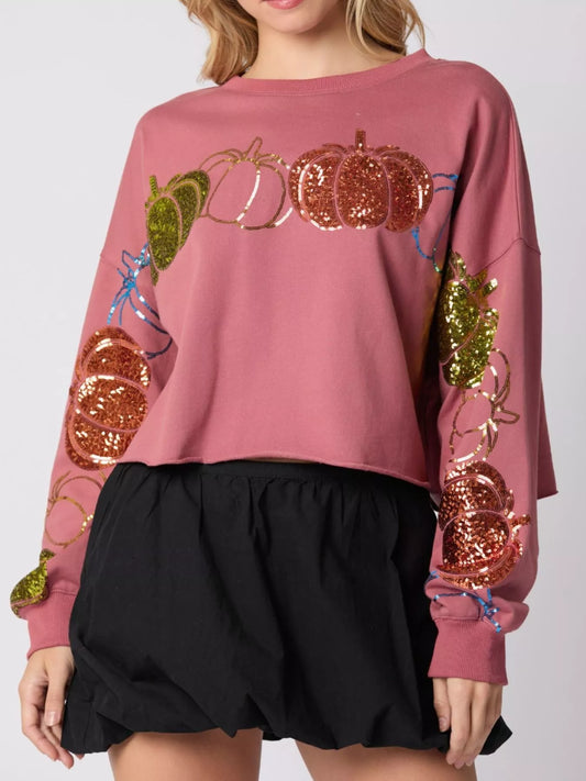 Pink sweatshirt with sequin pumpkins and leaves worn by a person on a white background