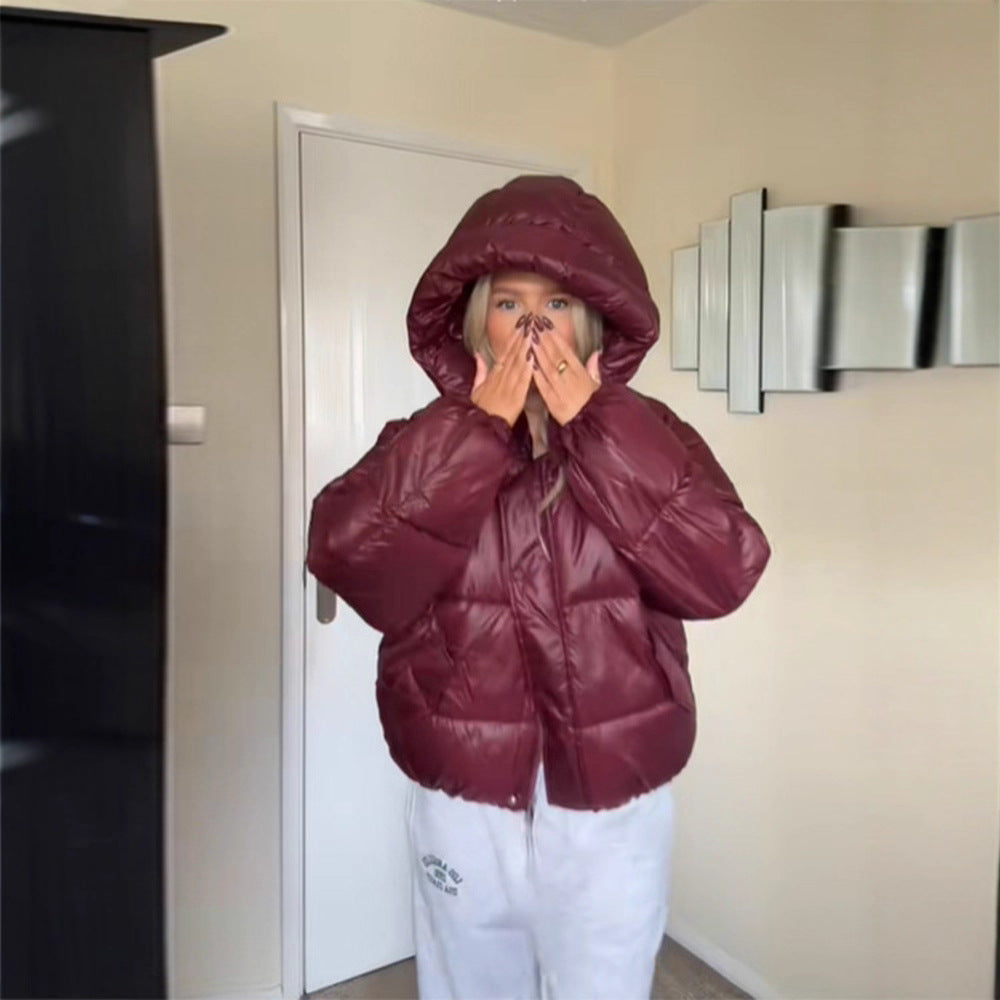 Person wearing a maroon puffer jacket in a room with a white door and light-colored walls.