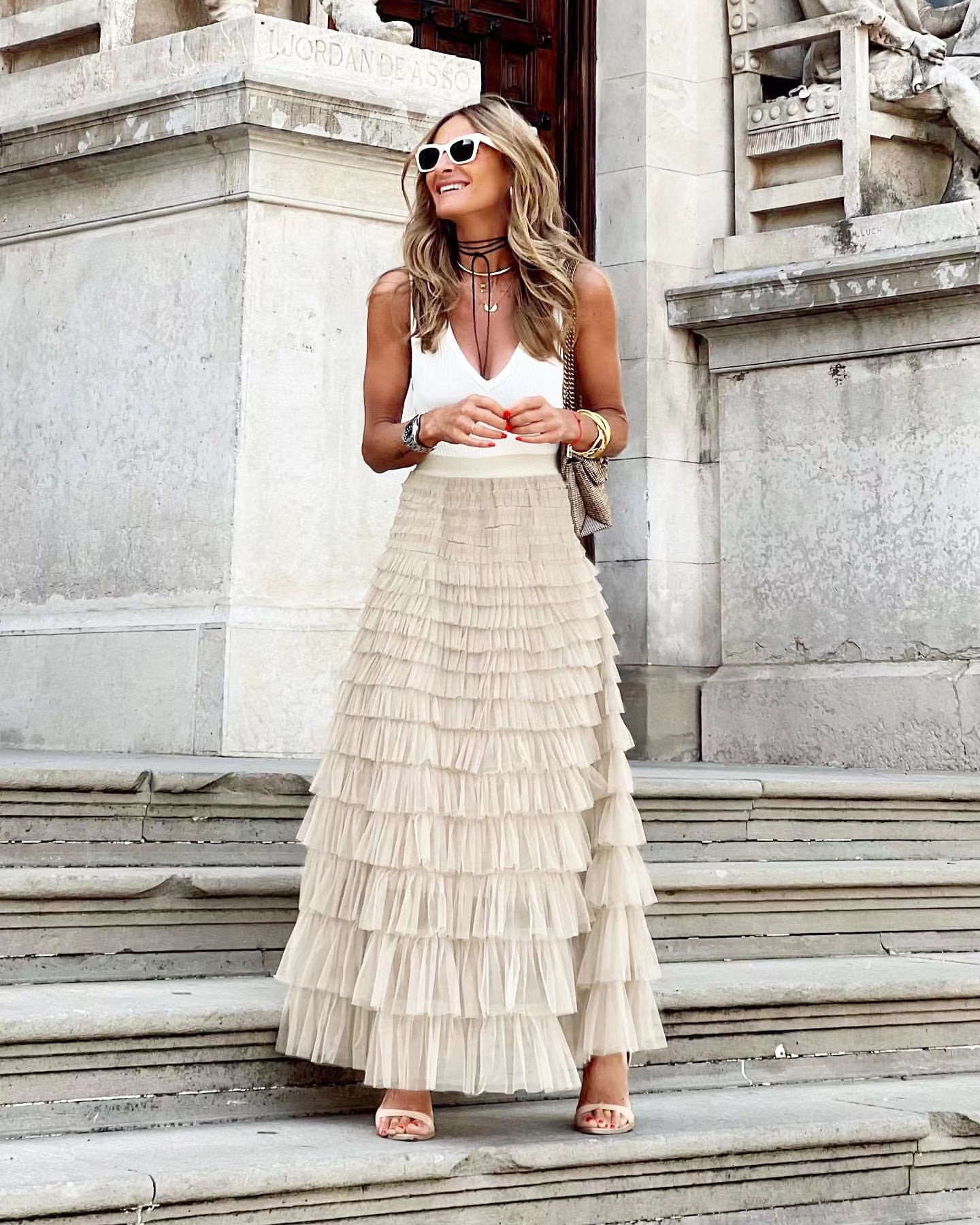 Woman wearing a white top and beige ruffled skirt standing on stone steps.