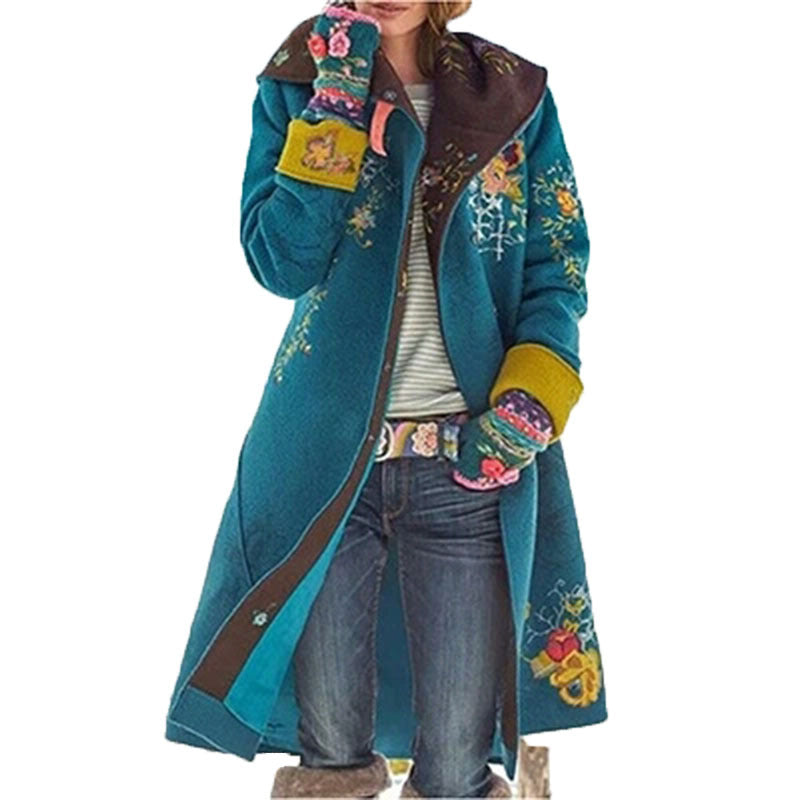 Person wearing a long teal coat with floral embroidery and colorful mittens on a white background