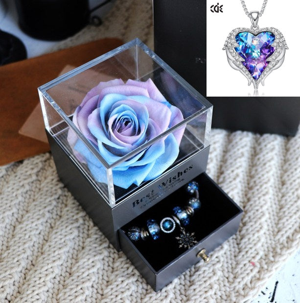 Glass box with a preserved rose and jewelry set on a textured surface