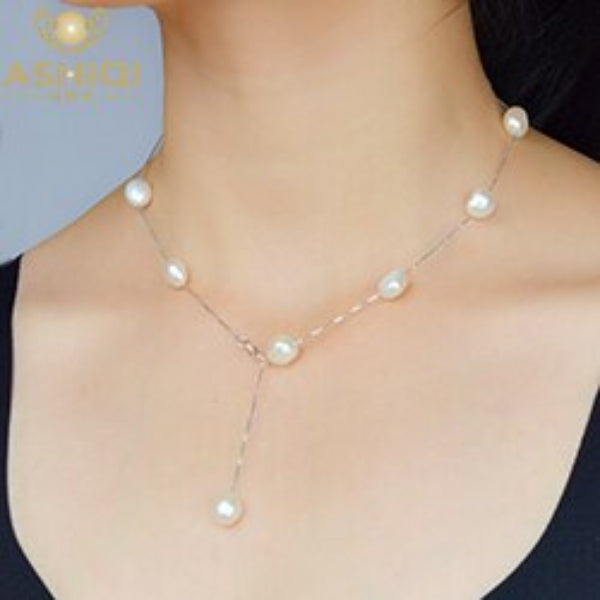 Pearl necklace on a person wearing a black top with a plain background