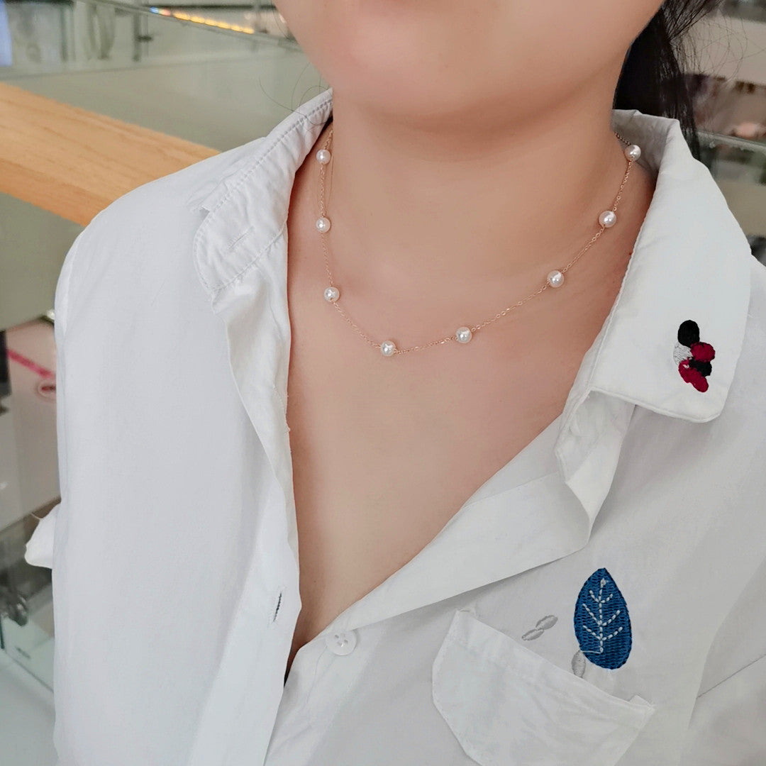 Person wearing a delicate pearl necklace with a white shirt in a blurred indoor setting