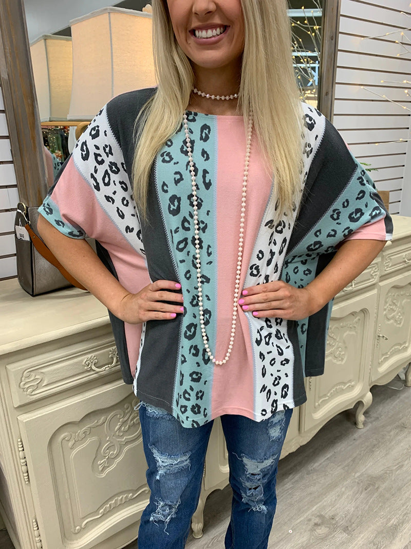 Woman wearing a leopard print cardigan over a pink top with blue jeans, standing indoors.