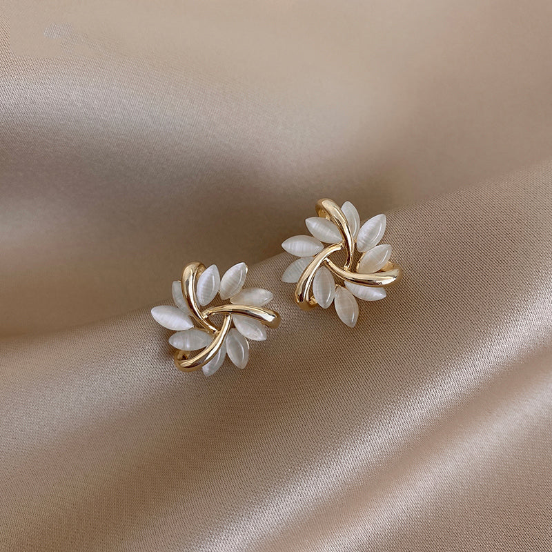 Pair of gold and white floral earrings on a beige fabric background