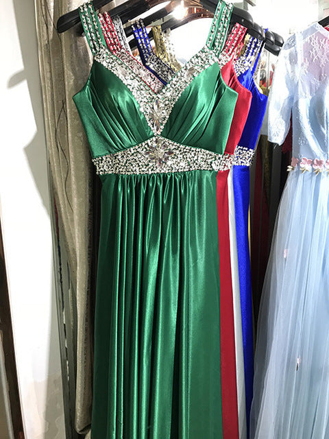 Green evening gown with embellishments on a hanger against a white wall.