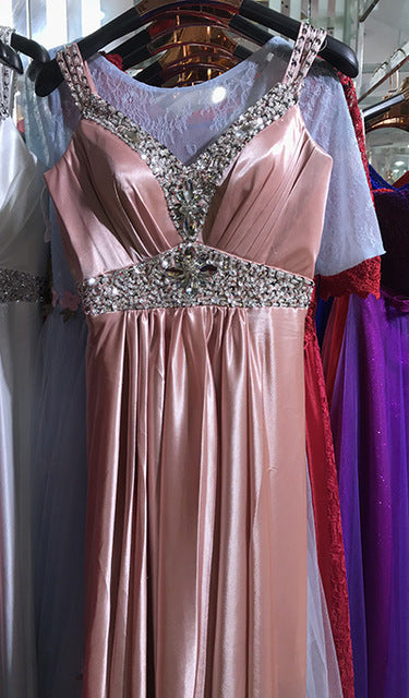 Pink evening gown with embellishments on a hanger against a blurred background of other dresses.