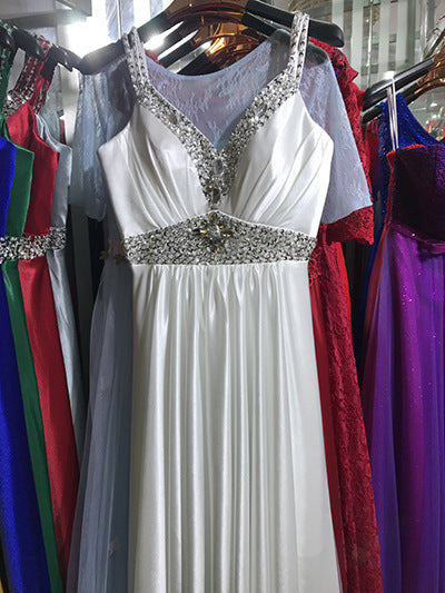 White evening gown with beaded details on a hanger surrounded by other colorful dresses.