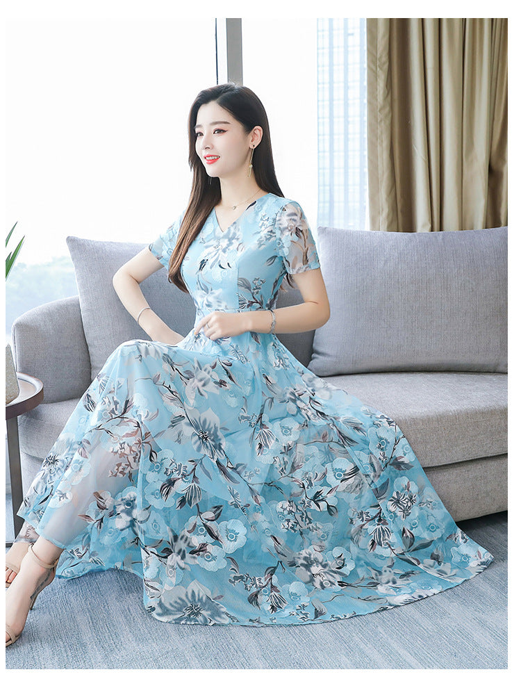 Woman in a blue floral dress sitting on a gray couch in a bright room.