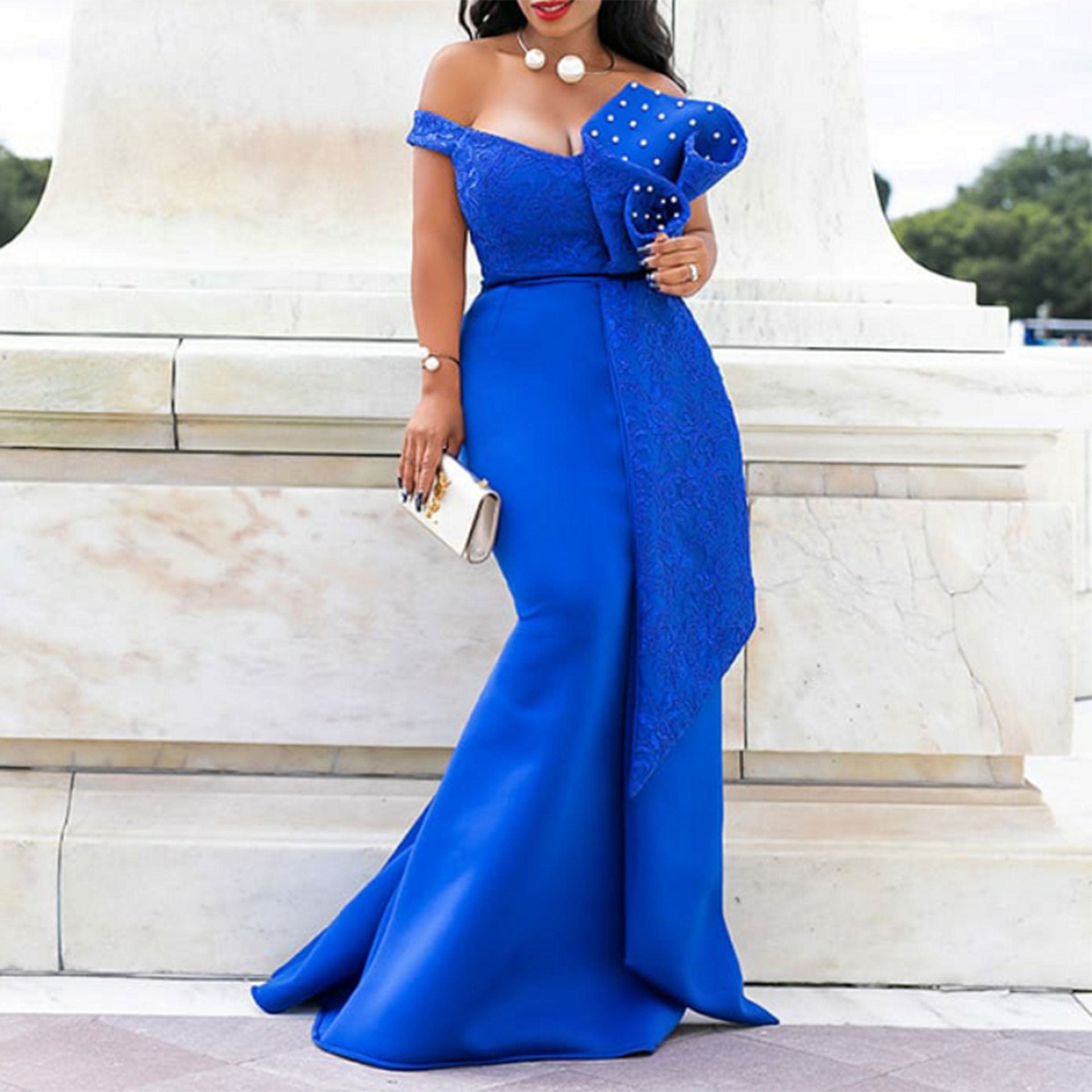 Woman in a blue off-shoulder dress holding a clutch in front of a marble building.