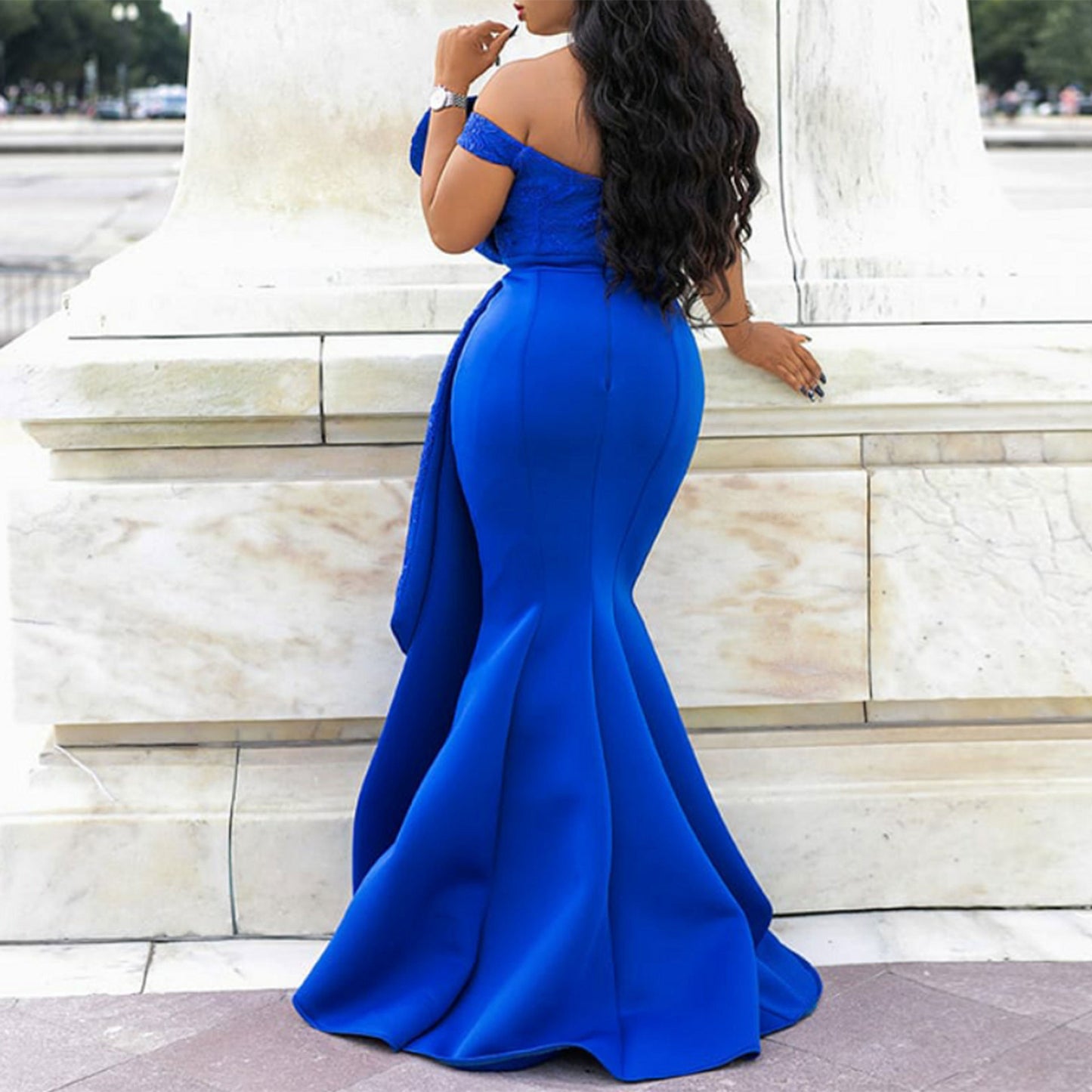 Woman in a blue evening gown standing against a marble wall.