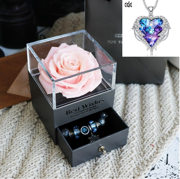Black gift box with pink rose, jewelry, and heart-shaped purple pendant on textured surface