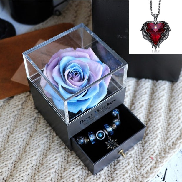 Glass box with a preserved rose and jewelry set on a textured surface
