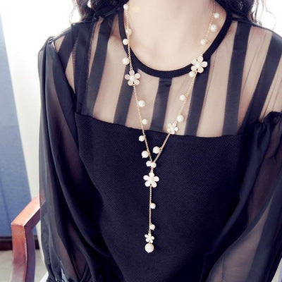 Mannequin wearing a black outfit with a long pearl necklace featuring white floral pendants.