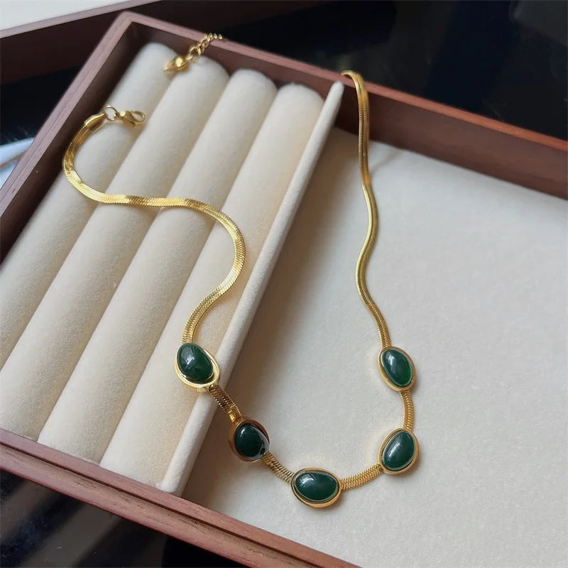 Gold necklace with green stones on a white cushion inside a wooden box