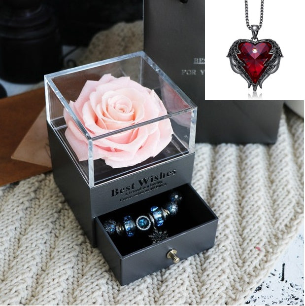 Black jewelry box with pink rose and necklace featuring red heart pendant on textured surface