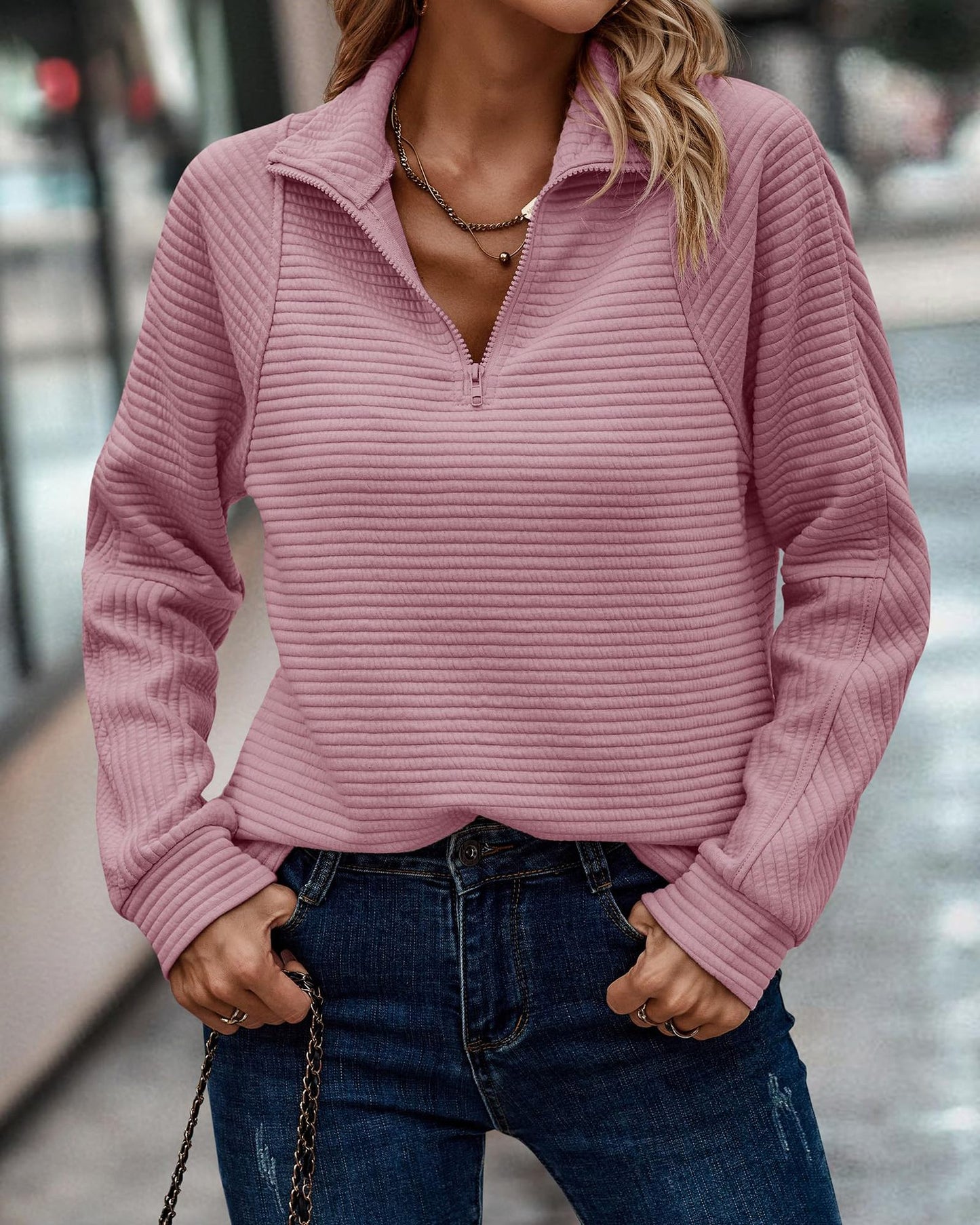 Person wearing a pink ribbed sweater and blue jeans outdoors.