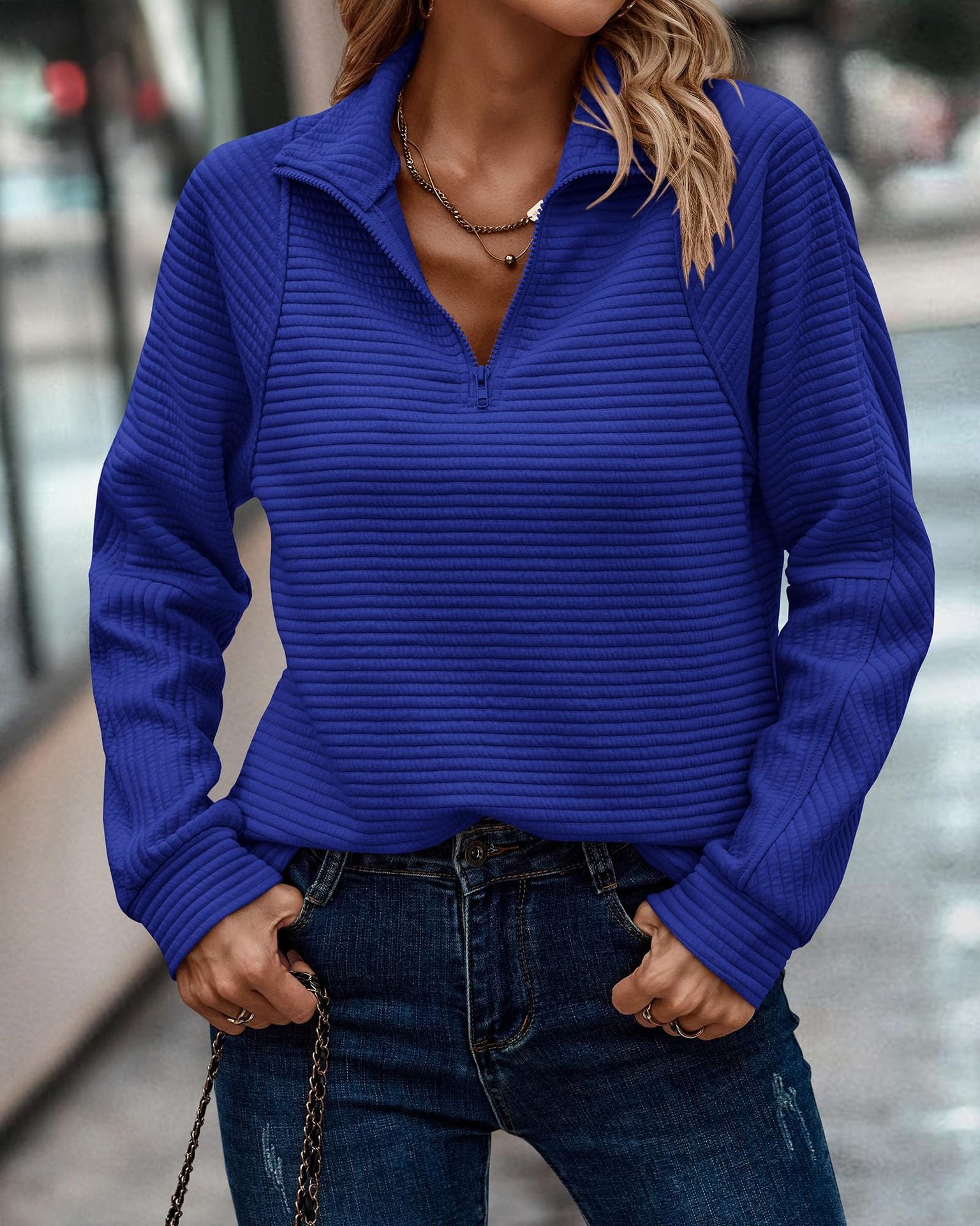 Person wearing a blue ribbed sweater and jeans in an urban setting