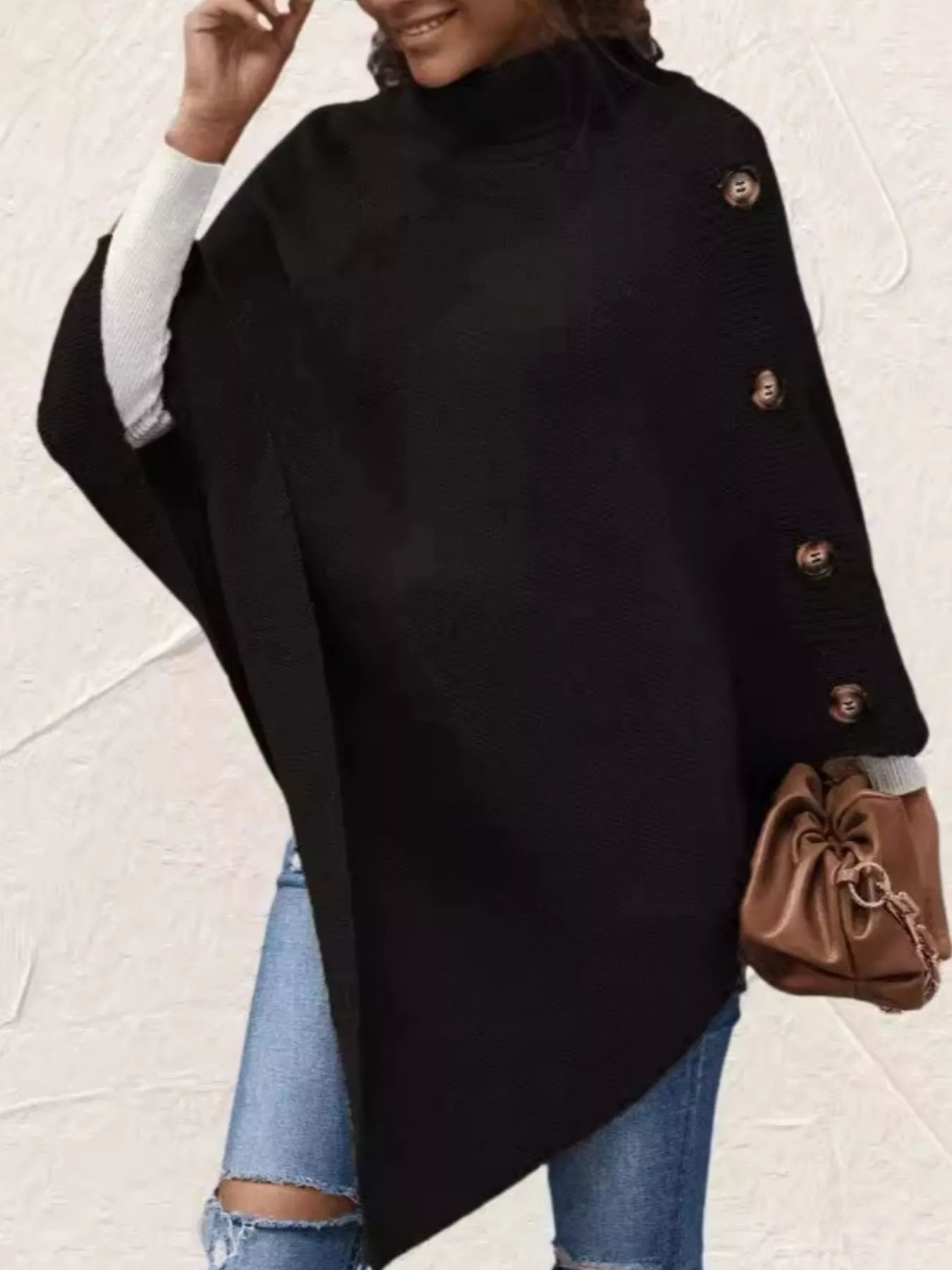 Person wearing a black poncho with gold buttons on a light background