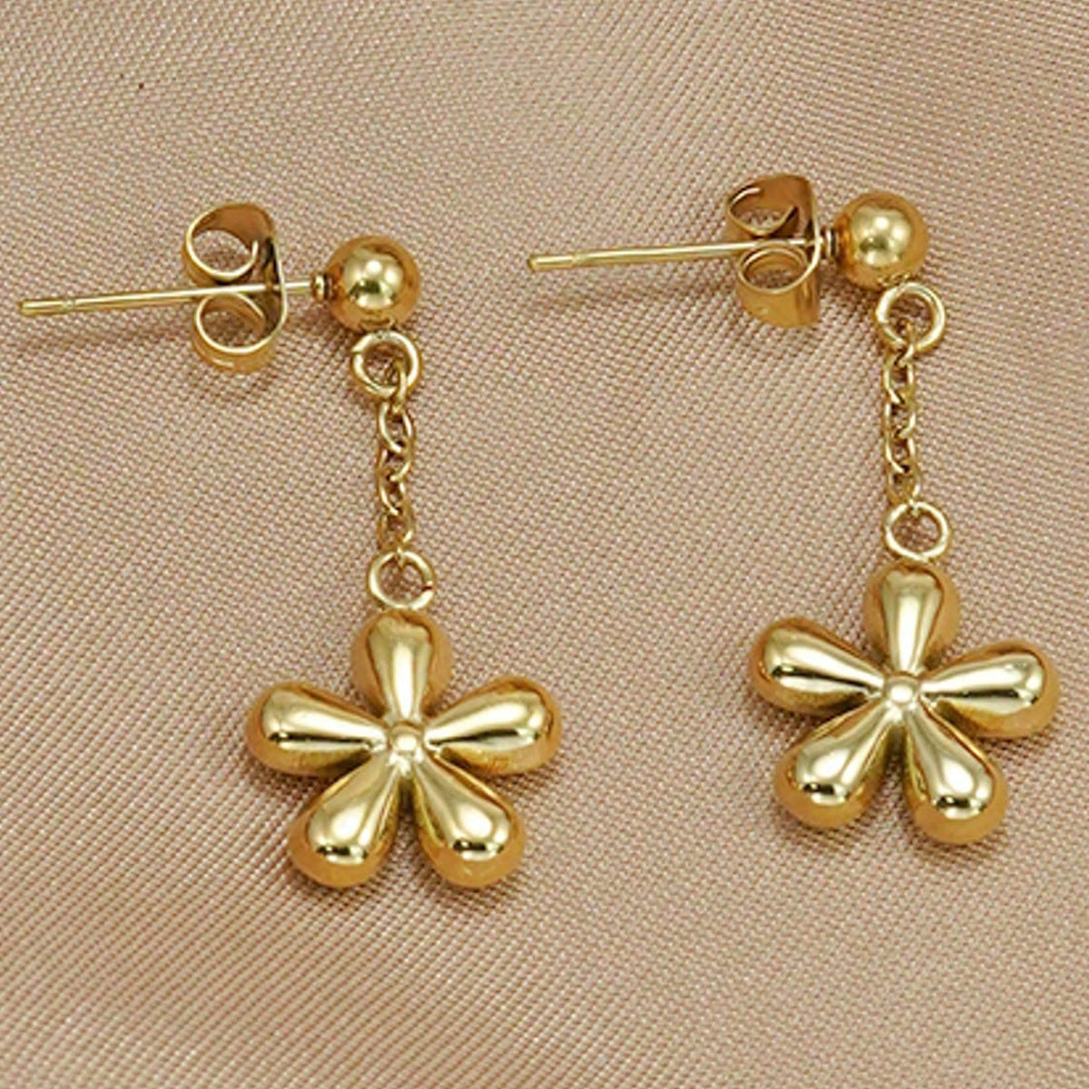Gold flower-shaped earrings on a beige background