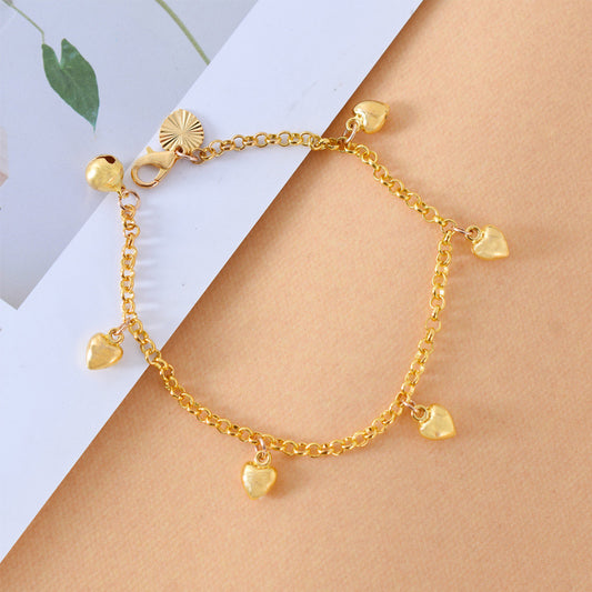 Gold anklet with heart-shaped charms on a person's ankle against a light background