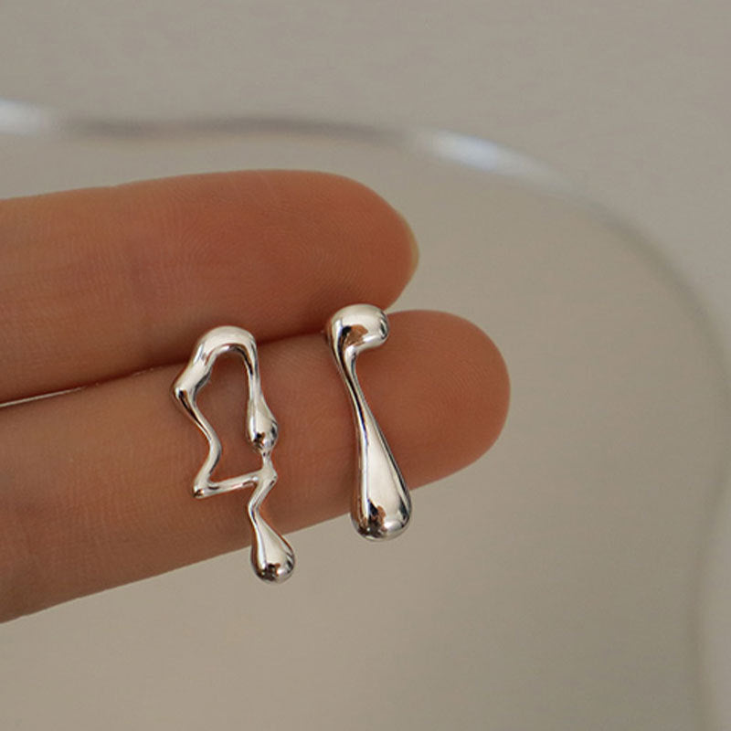 Silver earrings held between two fingers on a neutral background
