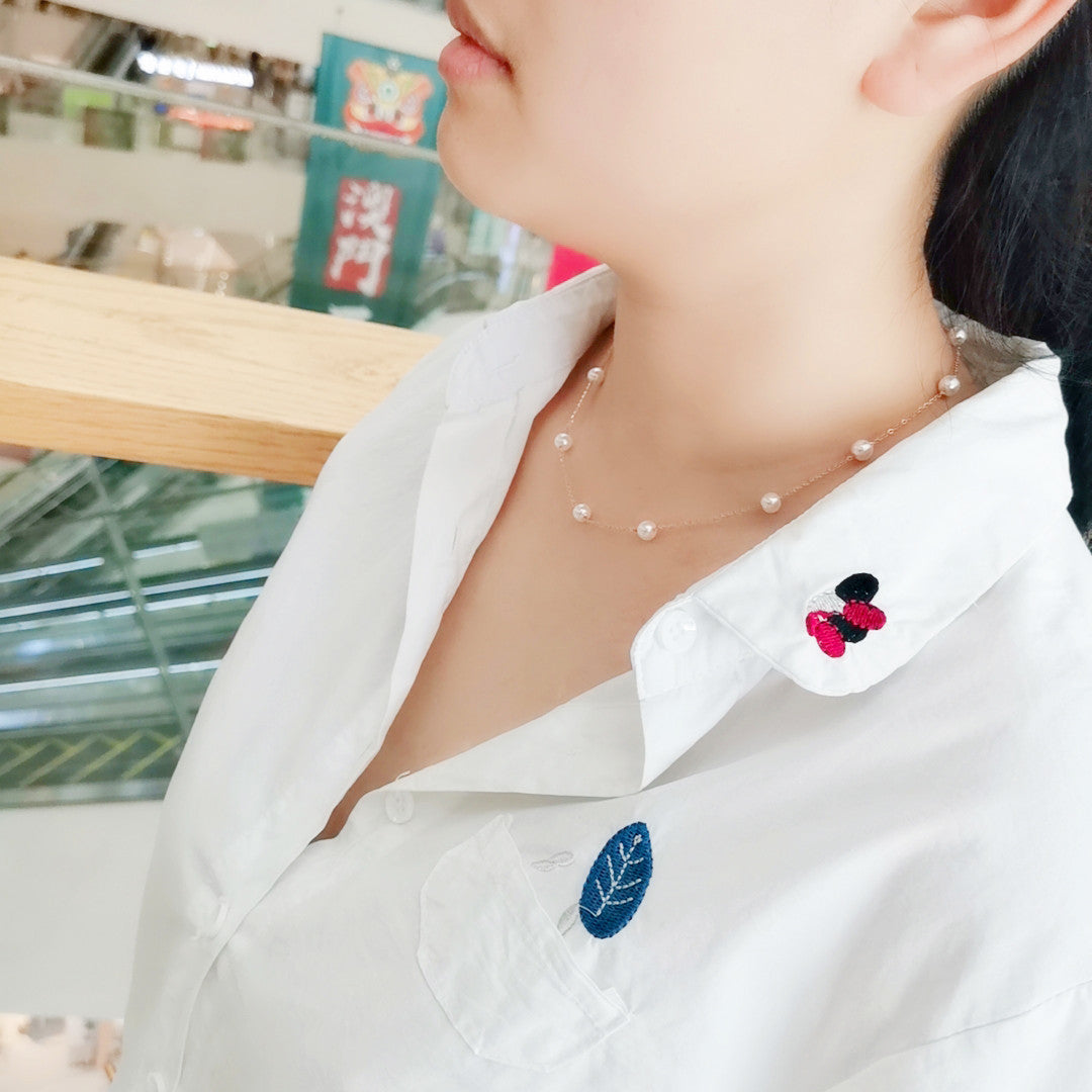 Person wearing a white shirt with floral embroidery and a pearl necklace.