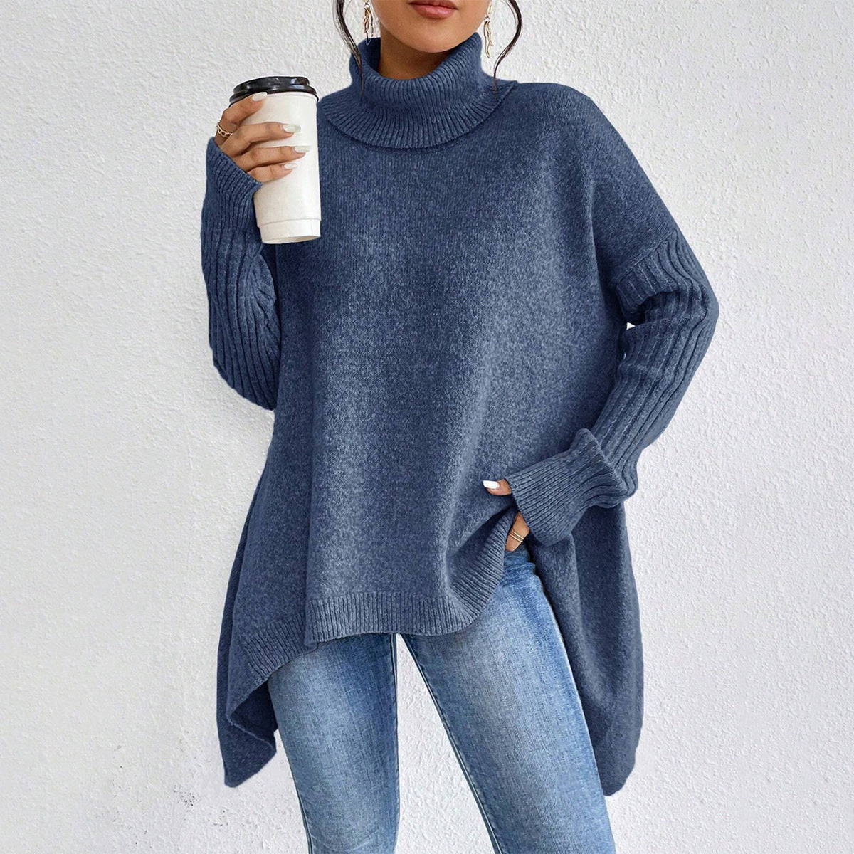 Person wearing a blue sweater and jeans holding a white cup against a light gray background