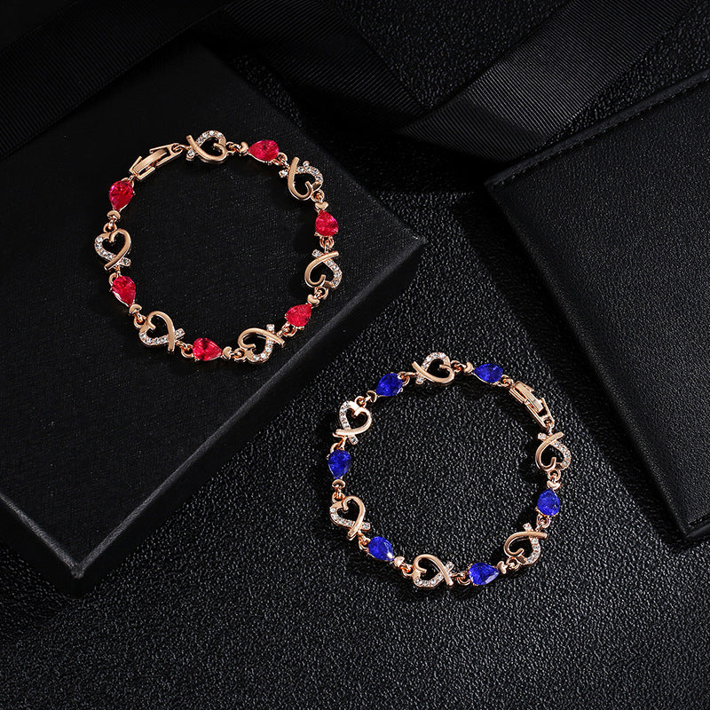Two gold bracelets with red and blue stones on a black surface