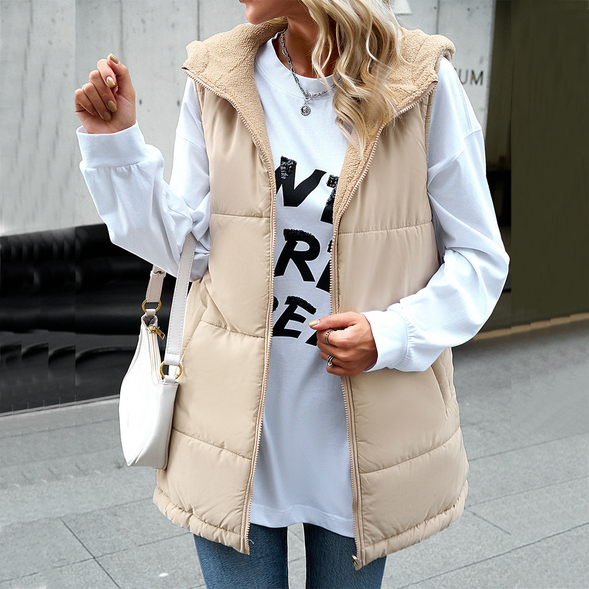 Person wearing a beige puffer vest over a white shirt with black text, standing on a street.
