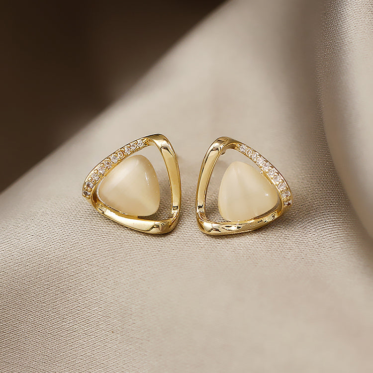 Gold earrings with white stones on a beige fabric background