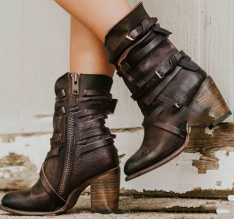 Brown leather boots with multiple straps and zippers on a rustic wooden floor.