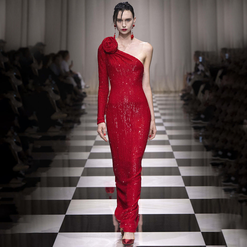 Model wearing a red one-shoulder dress on a fashion runway.
