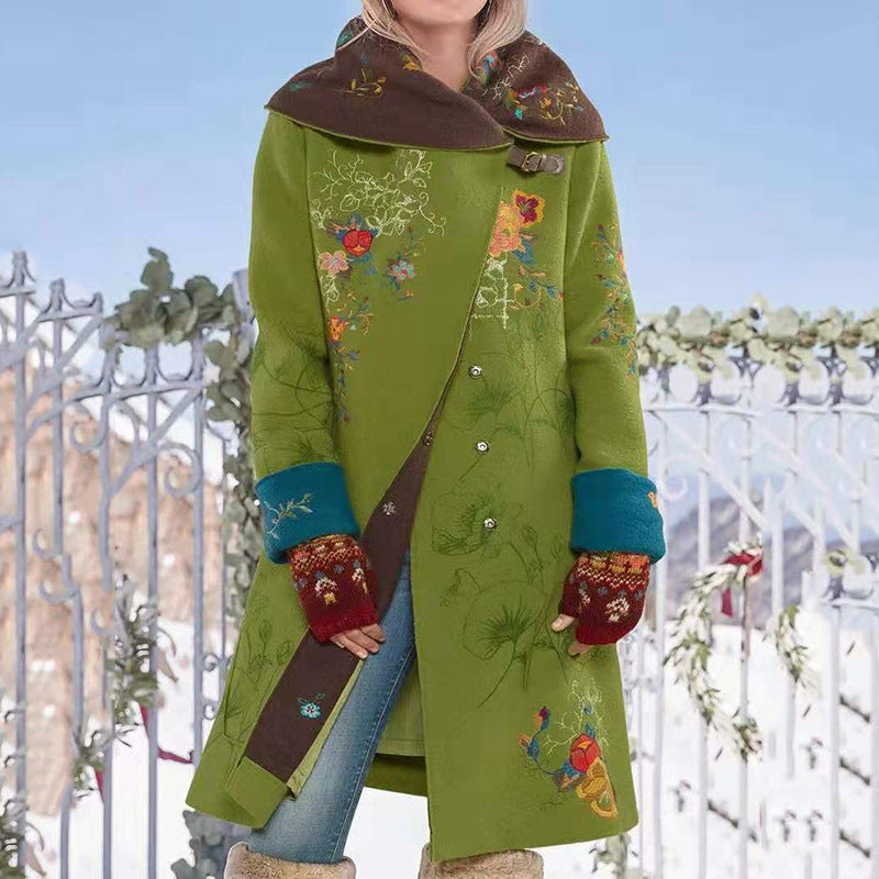 Person wearing a green coat with floral embroidery and brown collar, standing against a decorative metal gate.