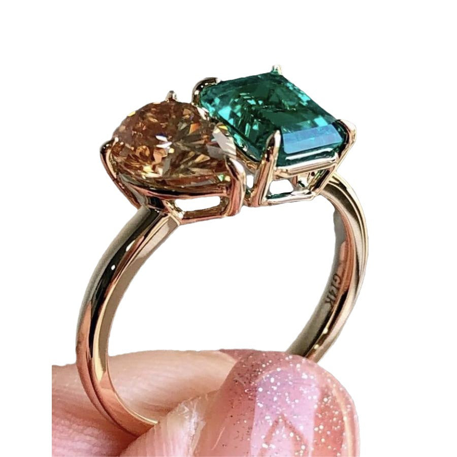 Rose gold ring with brown and green gemstones held by a hand with pink nail polish.