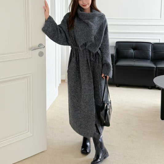 Woman in a long gray coat entering a room with a black sofa.