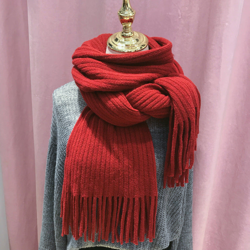 Red knitted scarf with fringe on a mannequin against a pink curtain background