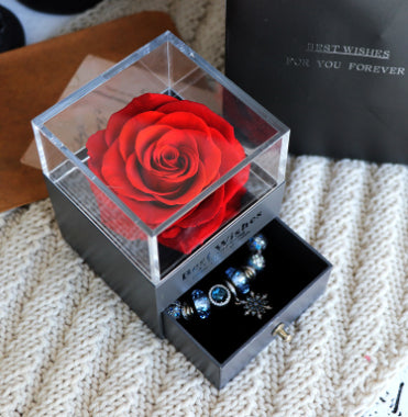 Red rose in a transparent box with jewelry inside on a textured surface