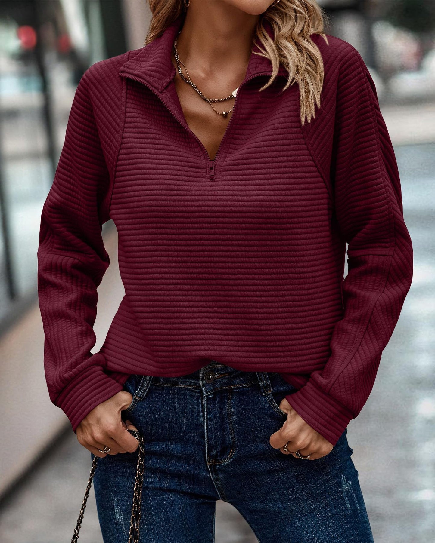 Person wearing a maroon ribbed sweater and blue jeans with a blurred background