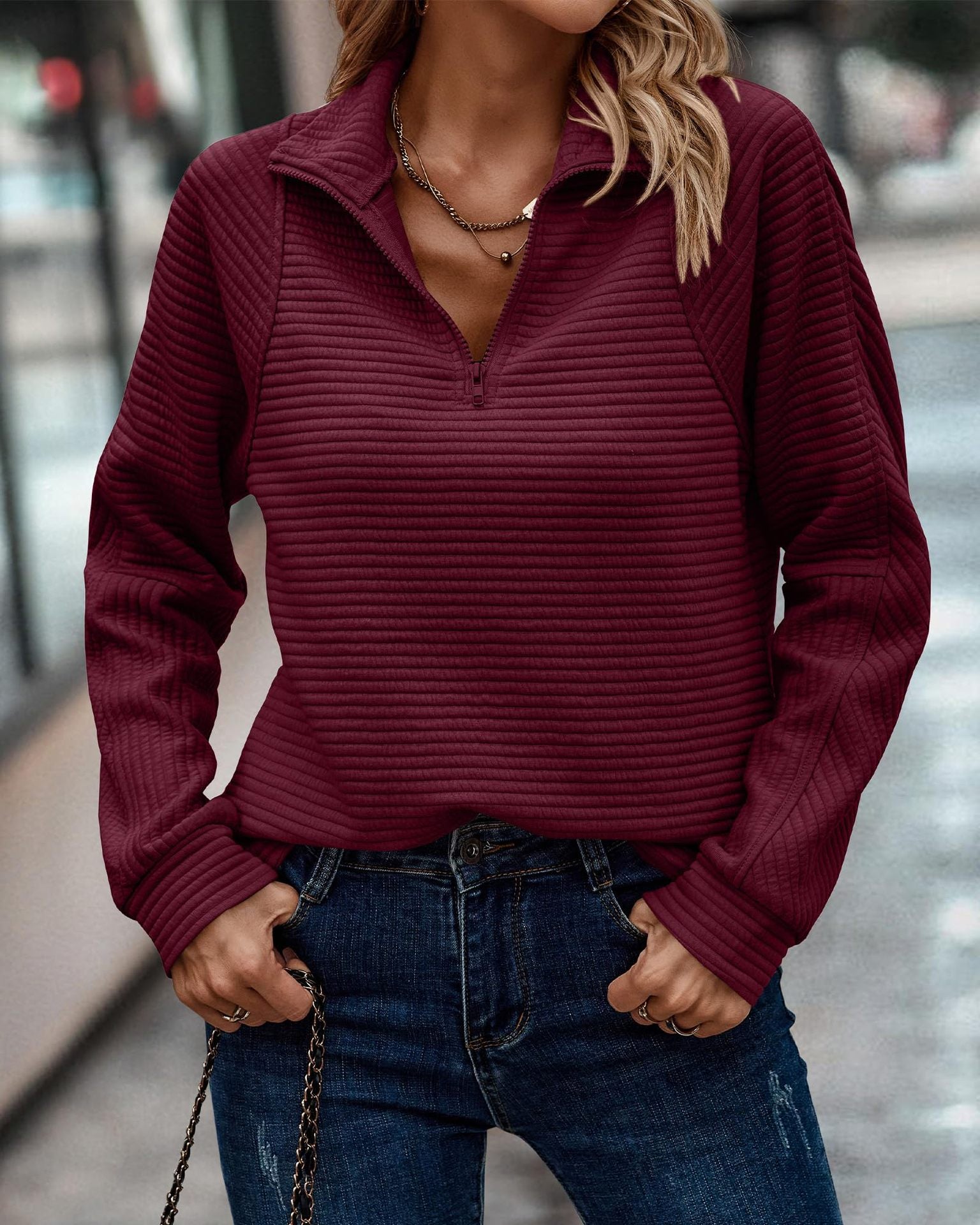 Person wearing a maroon ribbed sweater and blue jeans with a blurred background