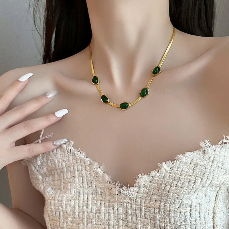 Woman wearing a gold necklace with green gemstones, touching her chest.