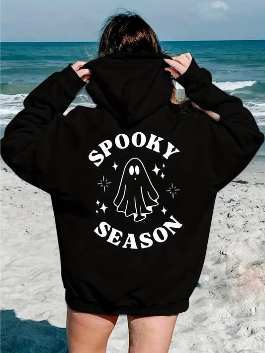 Person wearing a black hoodie with 'Spooky Season' print on a beach