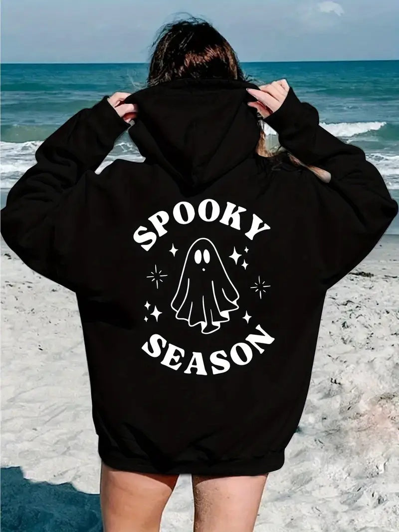 Person wearing a black hoodie with 'Spooky Season' print on a beach