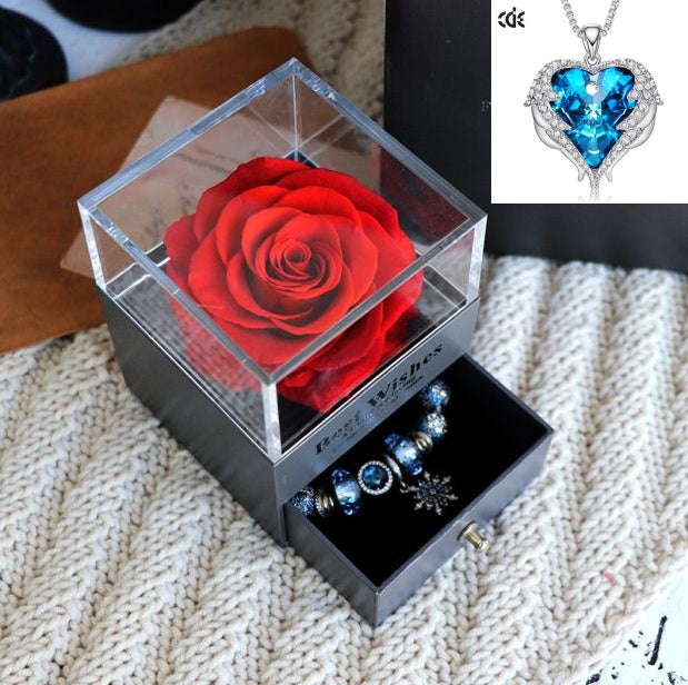 Clear box with a red rose and jewelry on a textured surface
