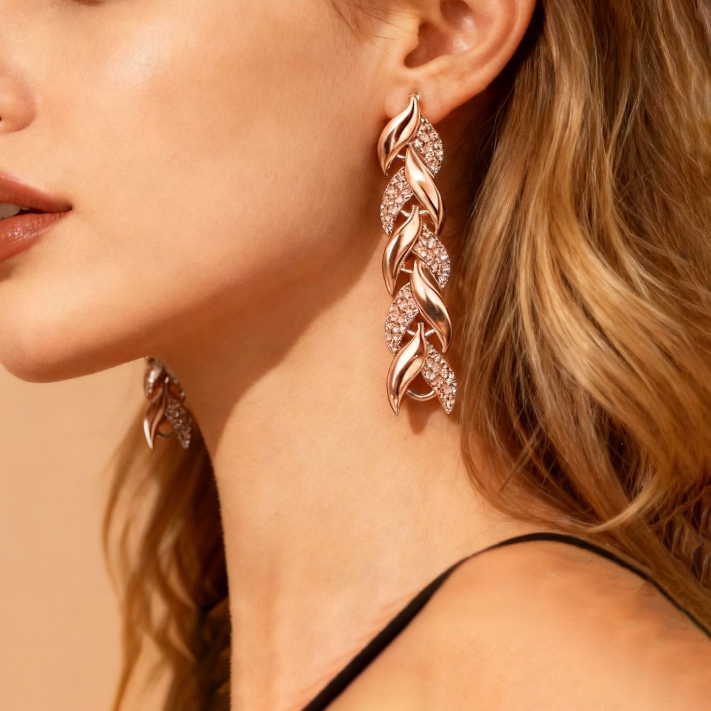 Close-up of a woman wearing rose gold braided earrings with clear stones.