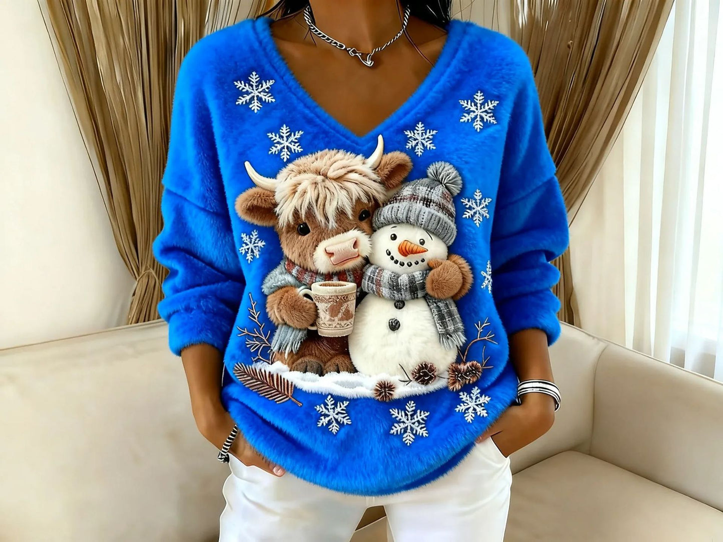 Blue sweater with Christmas-themed design featuring a cow and snowman, sitting on a beige couch.