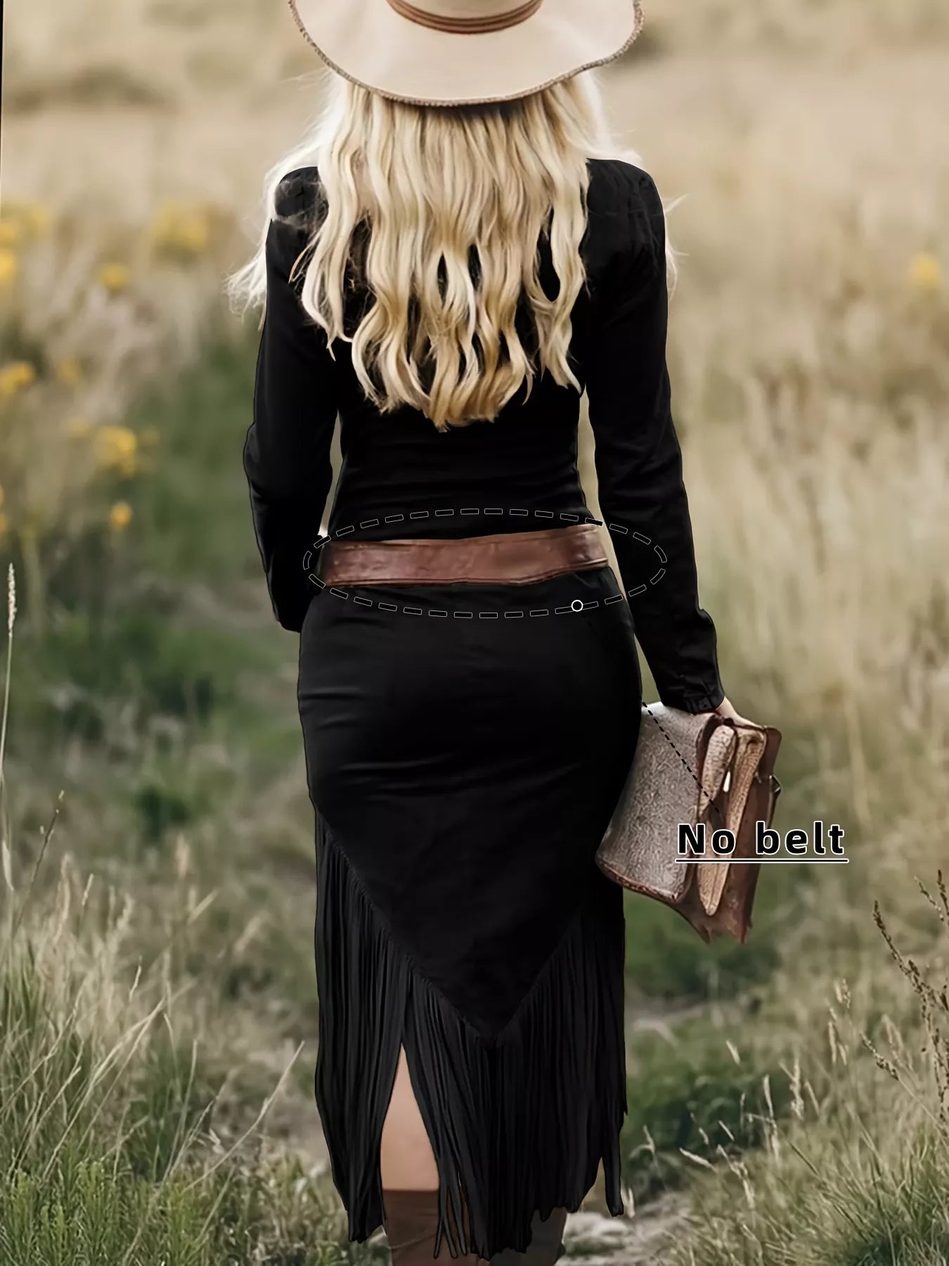 Person wearing a black outfit with a fringed skirt and wide-brimmed hat in a grassy field.