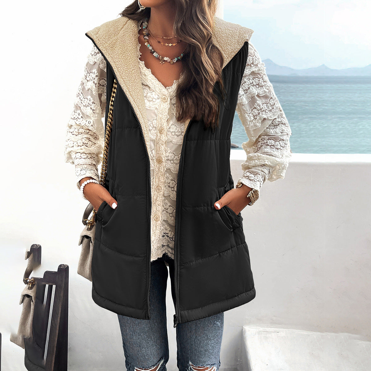 Person wearing a black puffer vest over a lace top with a scenic background