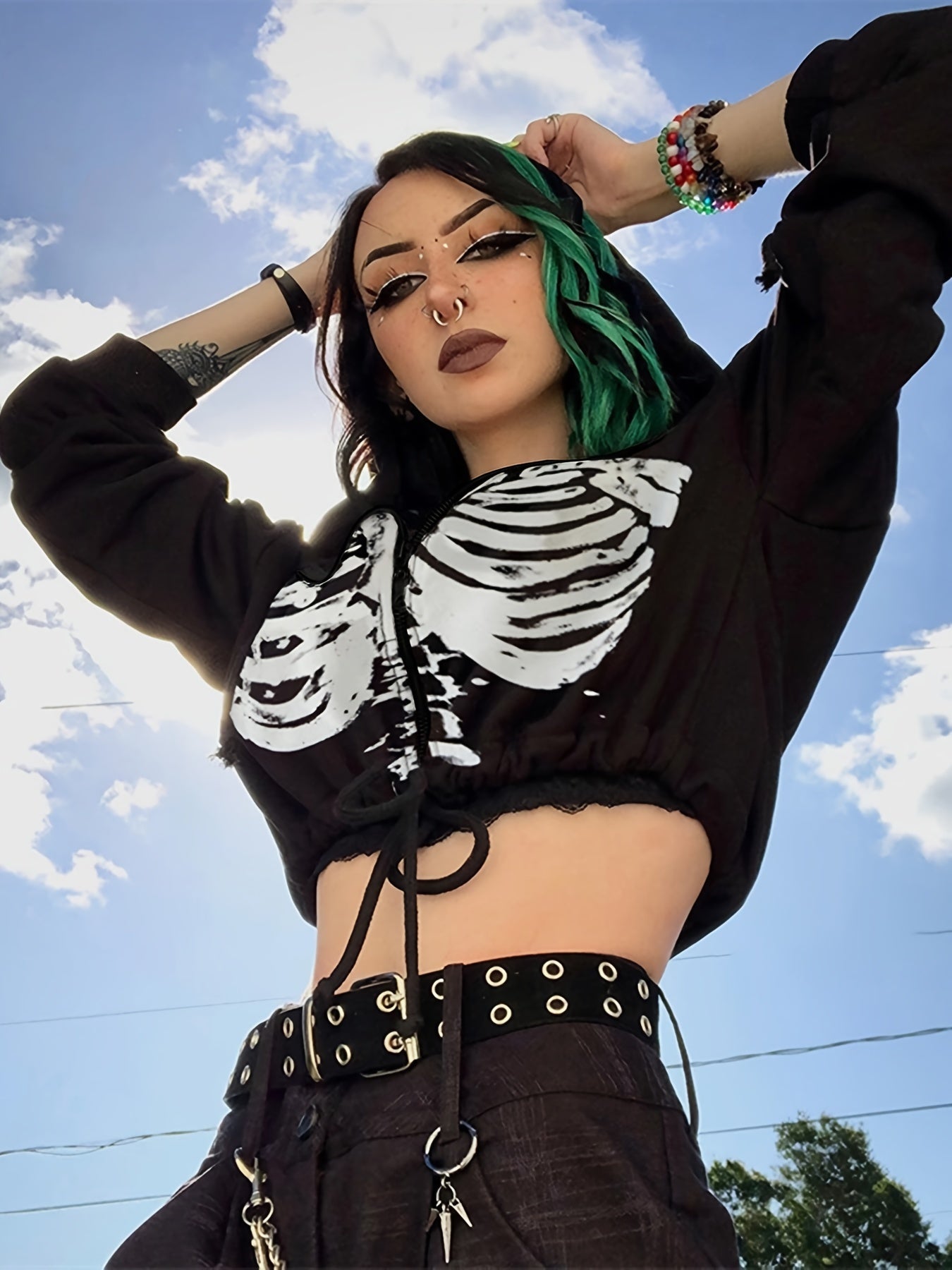 Person wearing a black crop top with skeleton design against a blue sky.